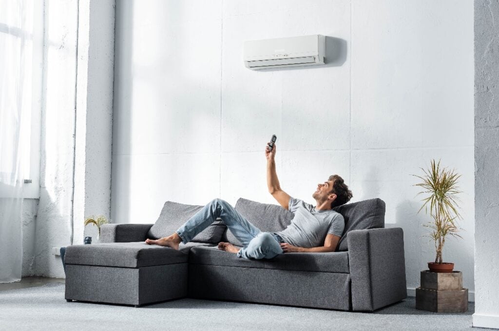 handsome man lying on sofa and switching on air conditioner